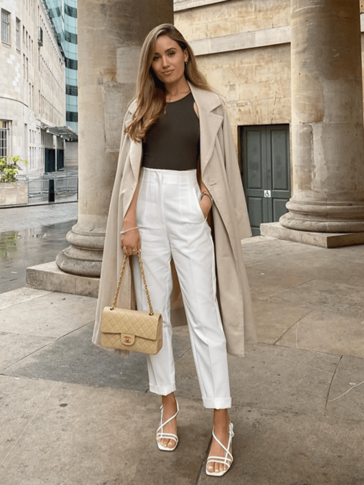 Woman dressed chic in trendy white dress pants with a long jacket draped over her shoulders, showcasing the latest styles from our Pants Collection.