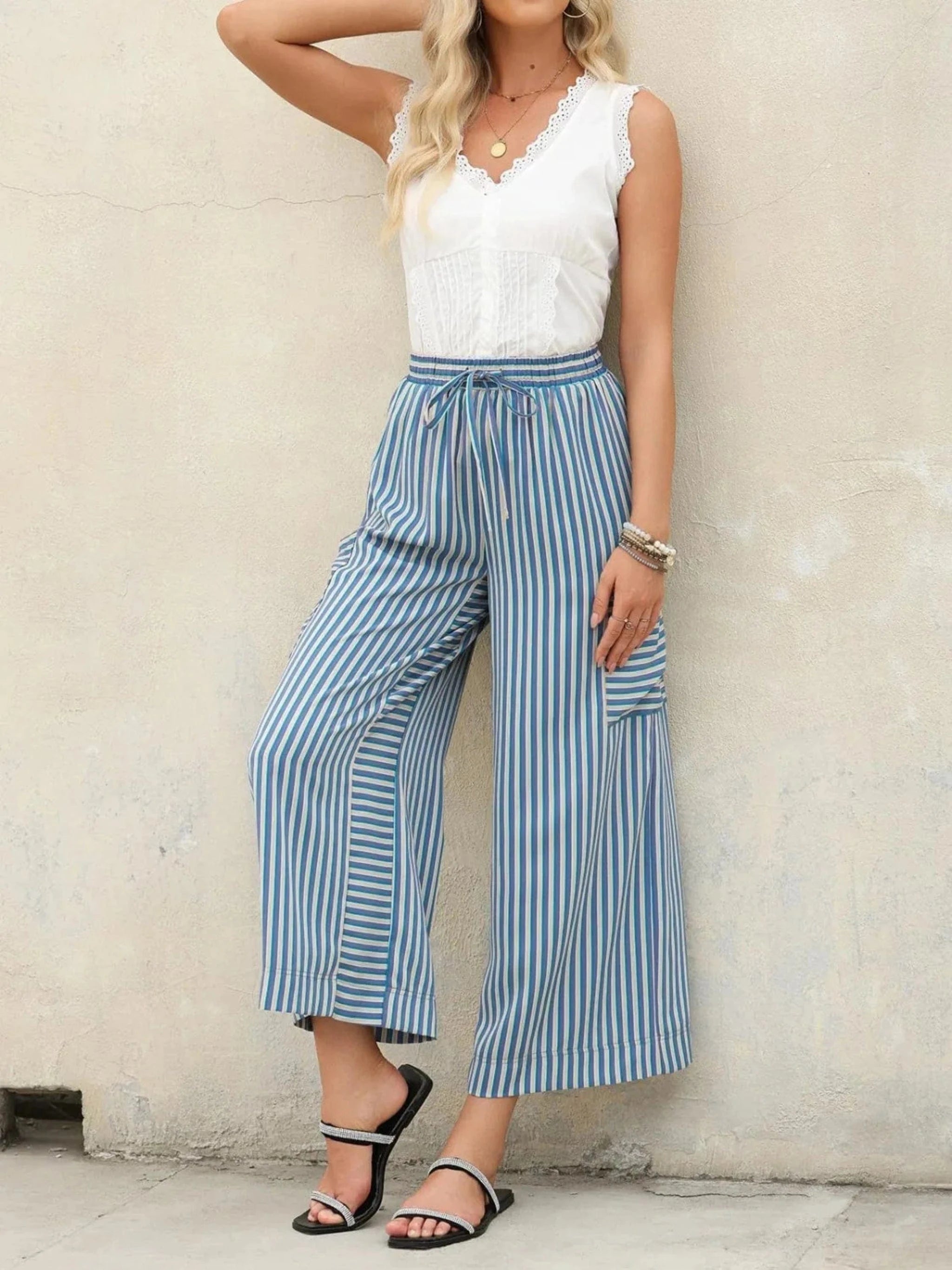 Model posing against a wall in striped blue summer trousers paired with a white top, showcasing the latest styles from our Trouser Trends collection.
