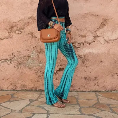 Woman wearing a black top and blue tie-dye pants standing against a textured pink wall.