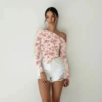 Woman wearing a floral off-shoulder top and white shorts against a plain background.
