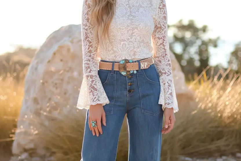Woman wearing a white lace top and blue jeans standing in a natural setting.