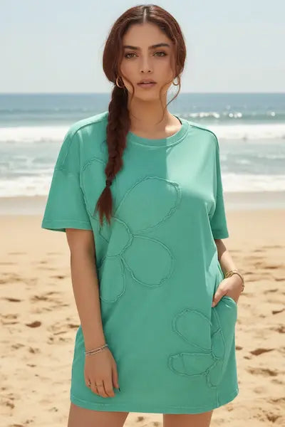 Woman wearing a teal dress with floral patterns on a beach.