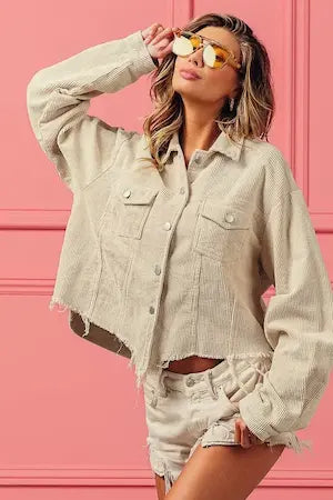 Woman wearing a light-colored denim jacket and shorts against a pink background.