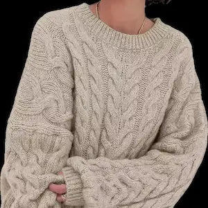 Beige cable knit sweater worn by a person on a black background.