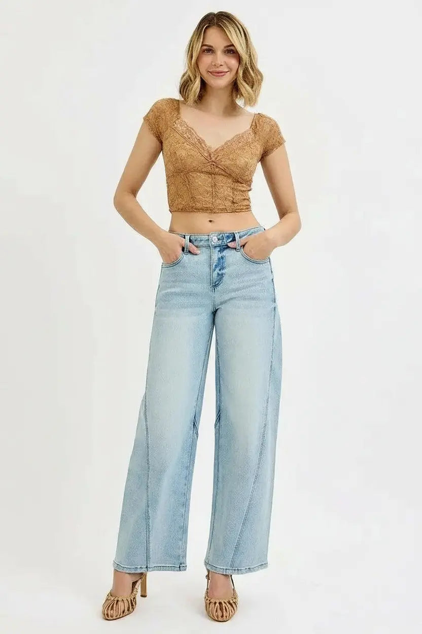 Woman wearing a brown lace top and light blue jeans on a white.