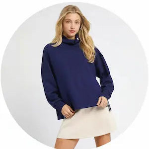 Woman wearing a navy blue sweater and white skirt on a white background.