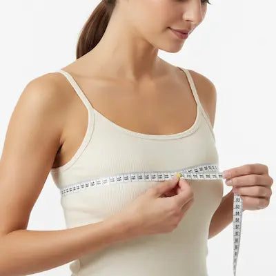 A woman measuring herself with a tape measure against a plain background.