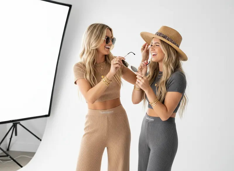 Two women in stylish outfits interacting in a photo studio setting.