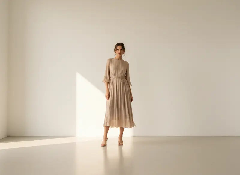 Woman in a beige dress standing in a minimalistic room with soft lighting.
