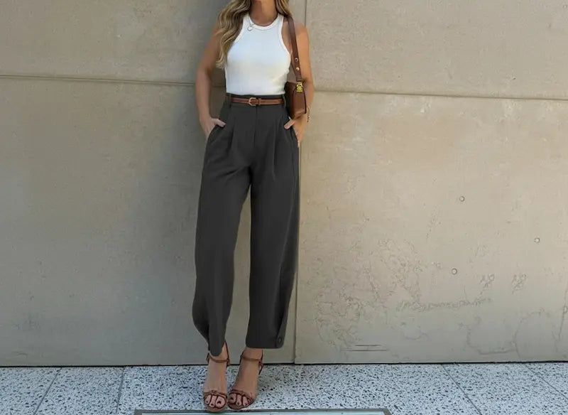 Woman wearing a white top and gray high-waisted pants against a beige wall.