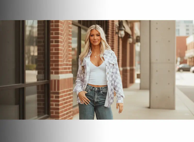 Woman standing on a city street wearing a white top, plaid shirt, and jeans.