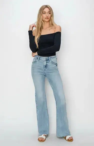 Woman wearing a black off-shoulder top and light blue jeans on a white background.