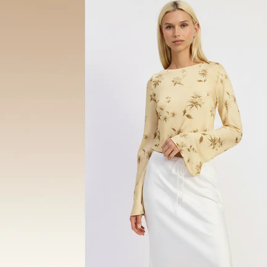 Woman wearing a yellow floral blouse and white skirt against a light background.