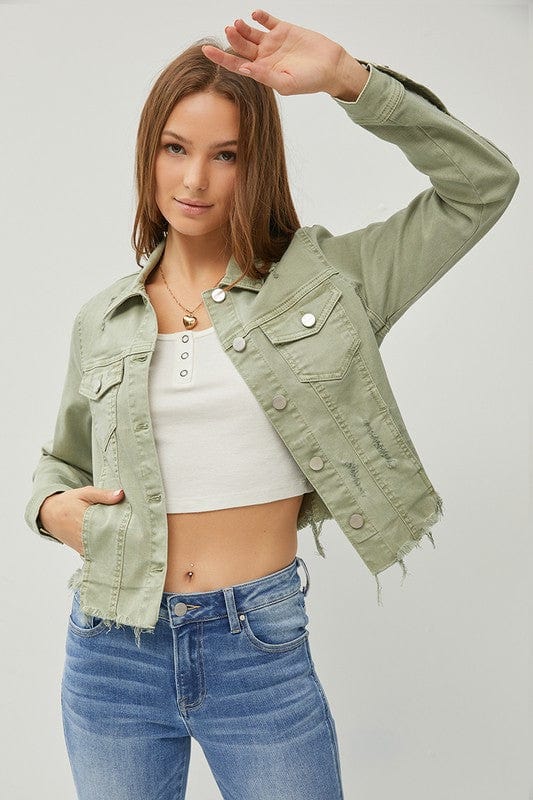 Woman wearing a light green denim jacket and blue jeans on a plain background.