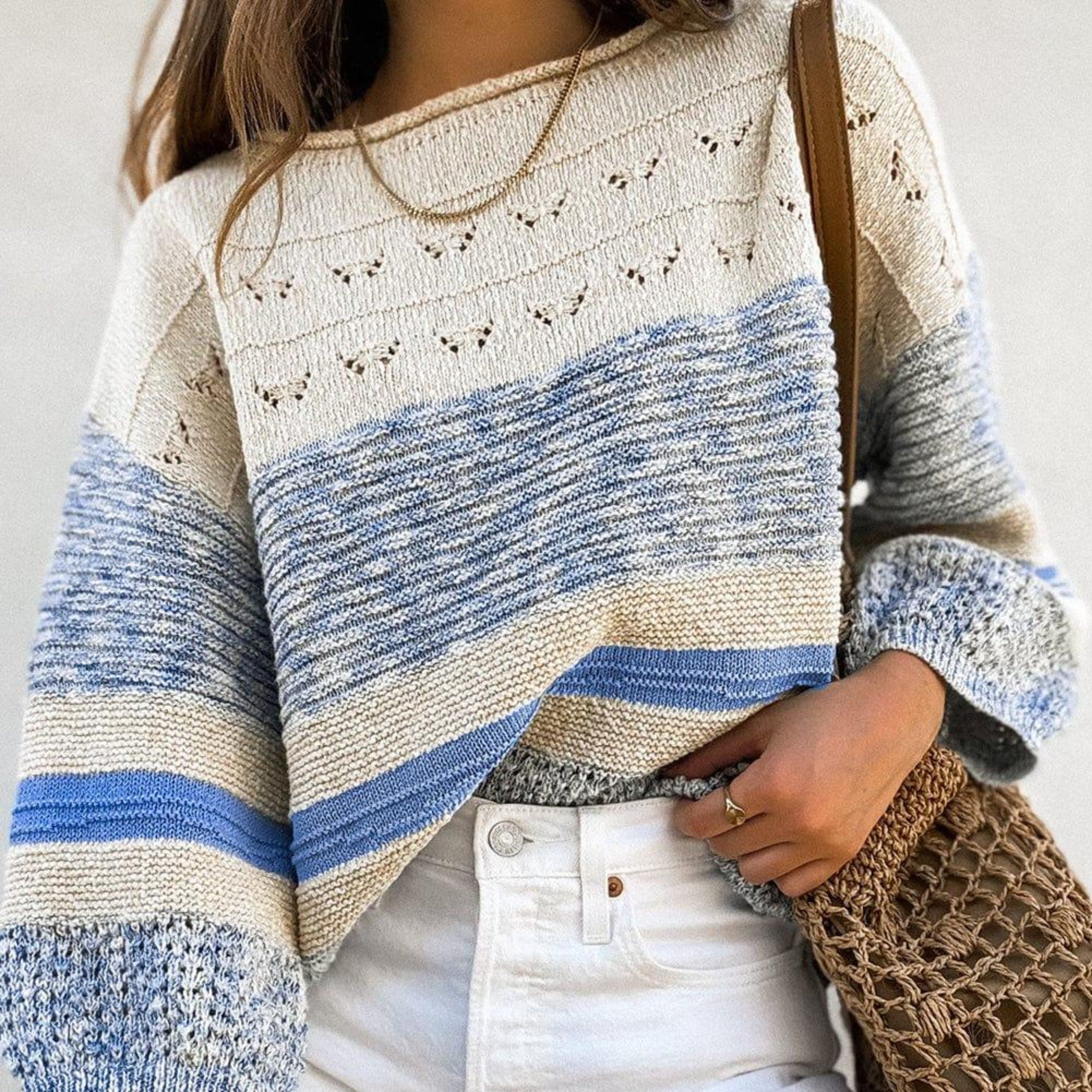 A model wearing a women's sweater from the sweater weather collection at the802Gypsy, showcasing off-white fabric with light blue soft-pattern stripes and soft textured designs with a solid, plain backdrop.